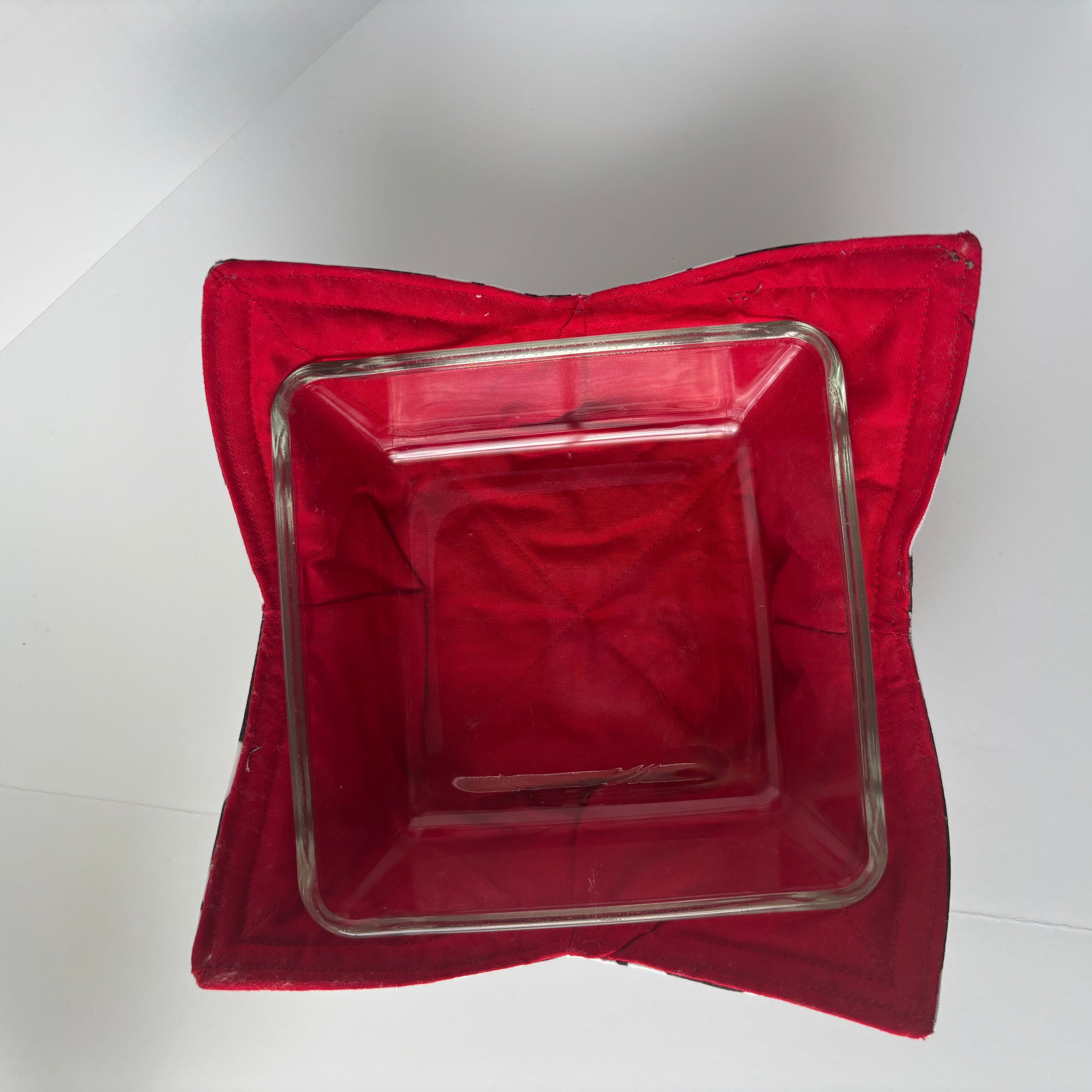 A square clear glass baking dish nested inside a red fabric cozy bowl. 