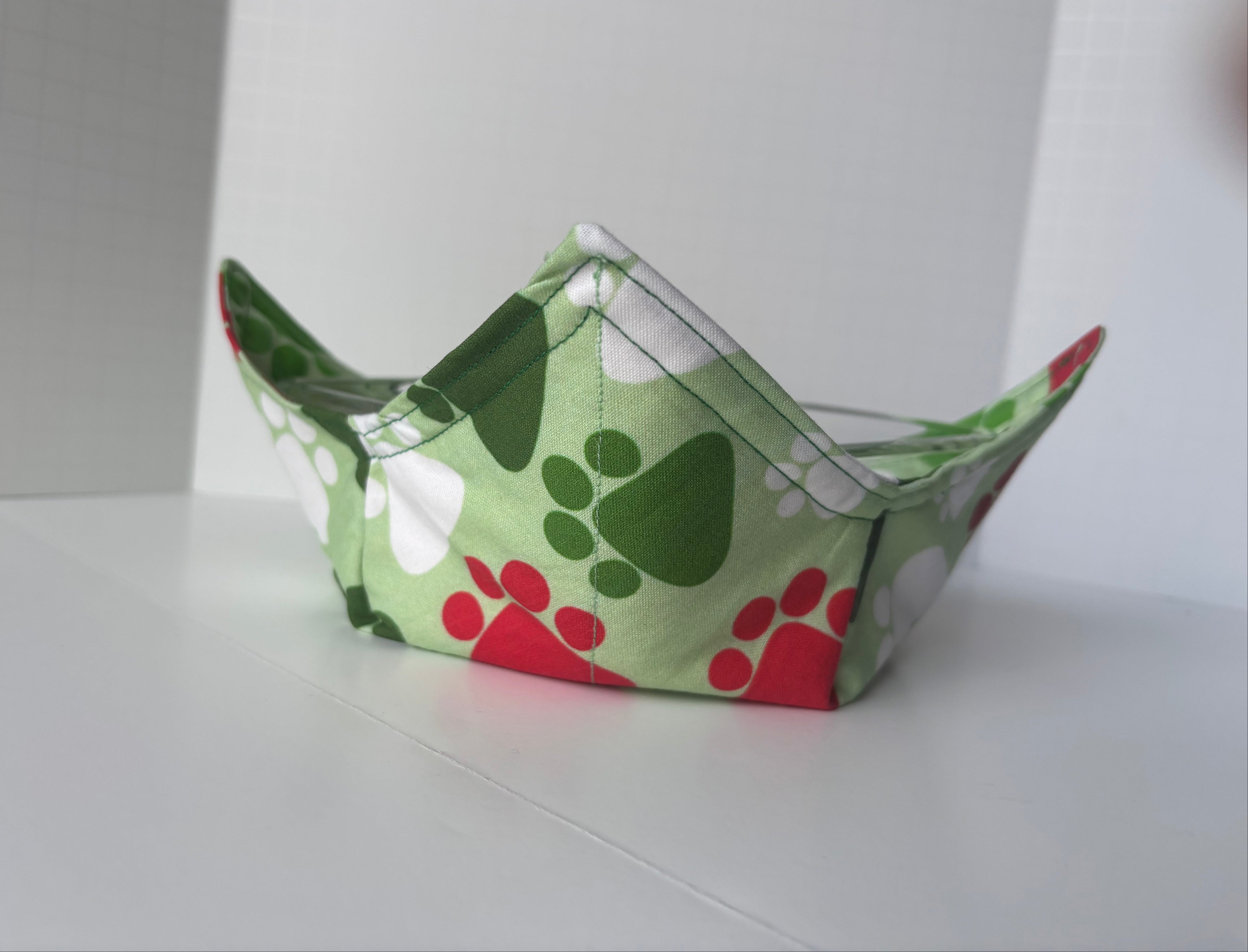 Green fabric bowl with paw print pattern on a white surface