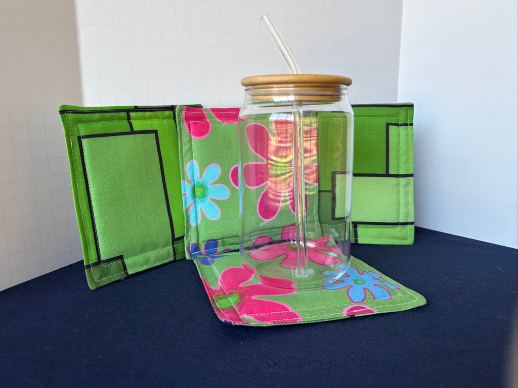 Clear glass tumbler with floral design on a green floral holder against a white background