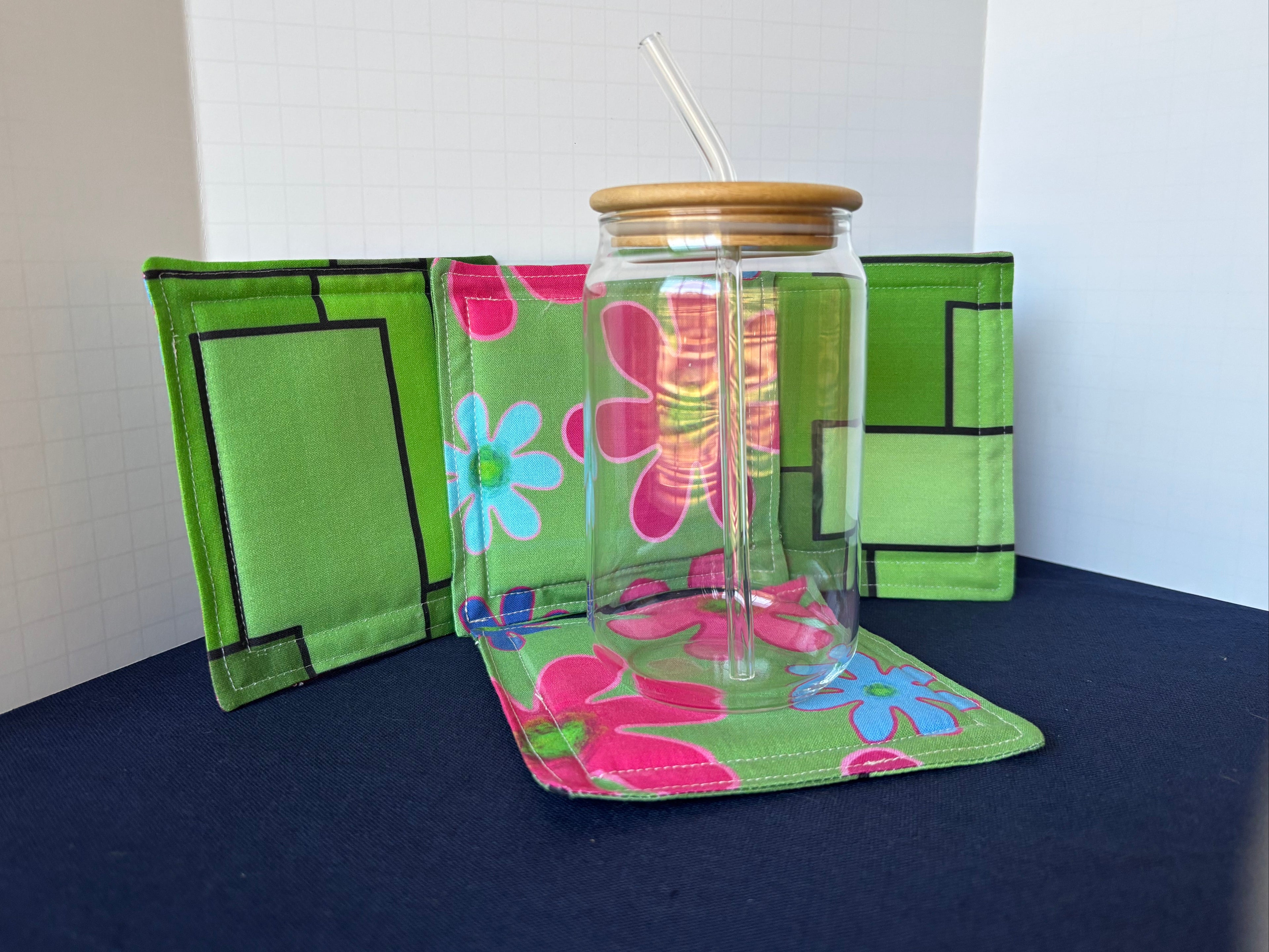Clear glass tumbler with floral design on a green floral holder against a white background