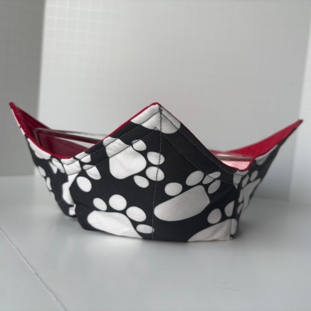 Fabric cozy bowl with paw print patternon the outside with a red fabric on the inside on a white background