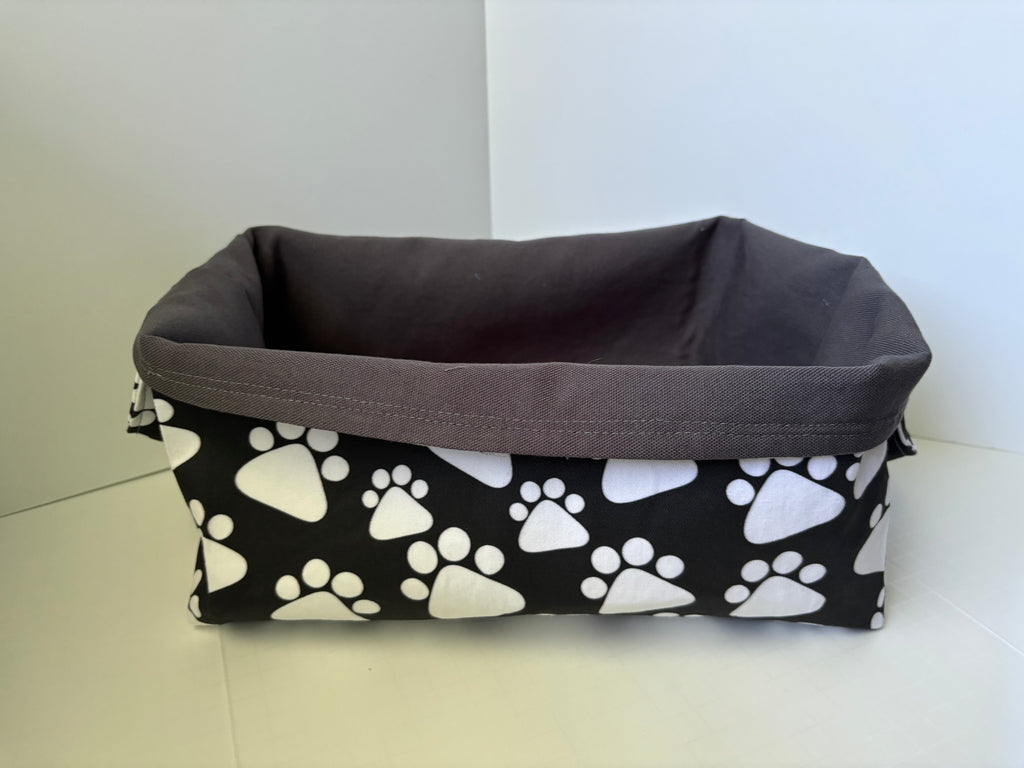 A rectangular fabric basket with a dark grey interior featuring a black and white paw print pattern, set against a plain light background.