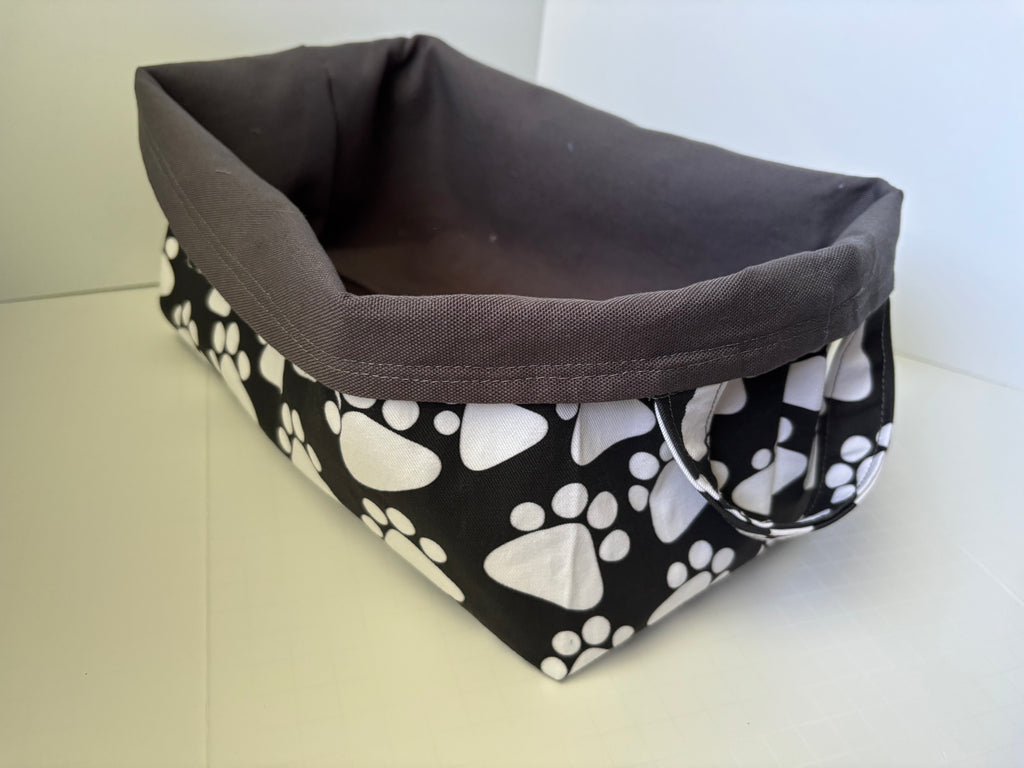 A rectangular fabric basket with a dark gray interior and exterior sides featuring a black and white paw print pattern, shown on a light-colored surface.