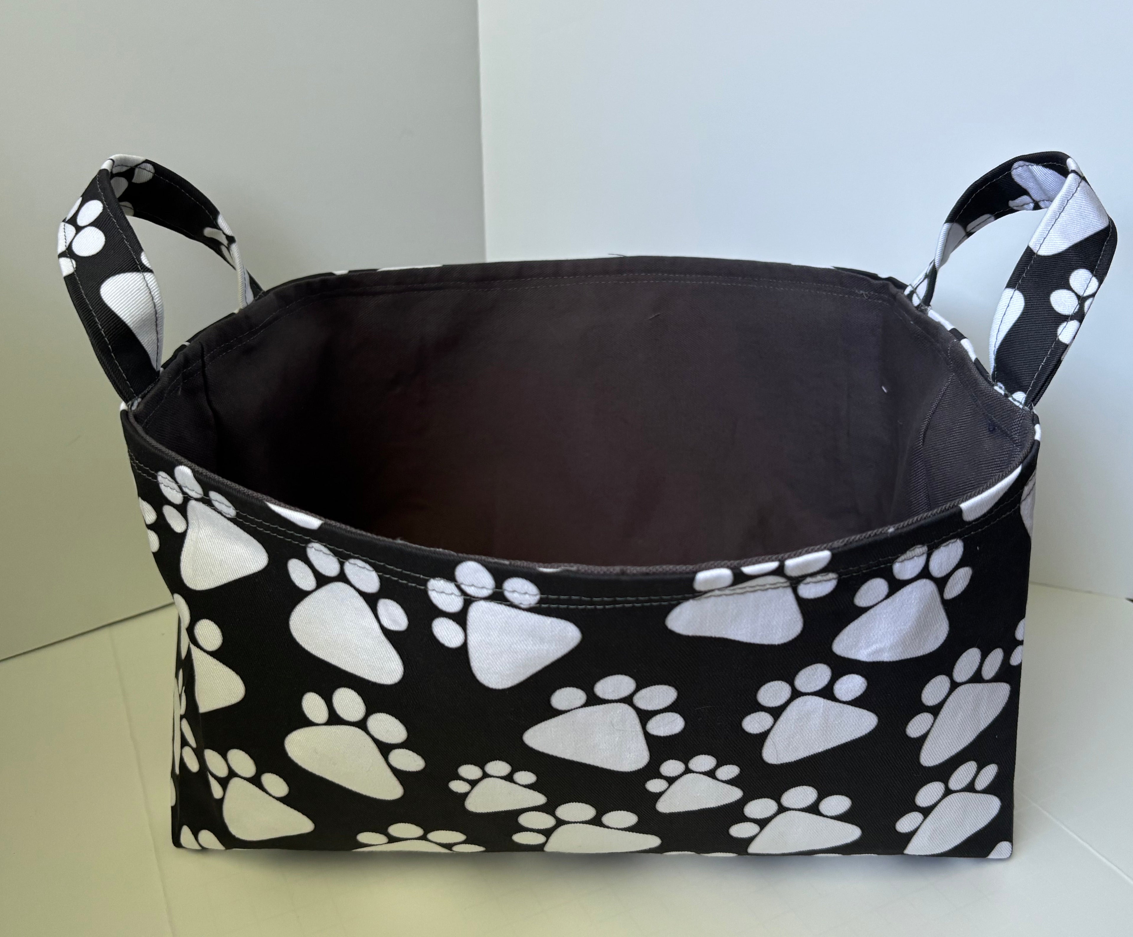 A fabric storage basket with a black and white paw print pattern, featuring two side handles and a dark gray interior.