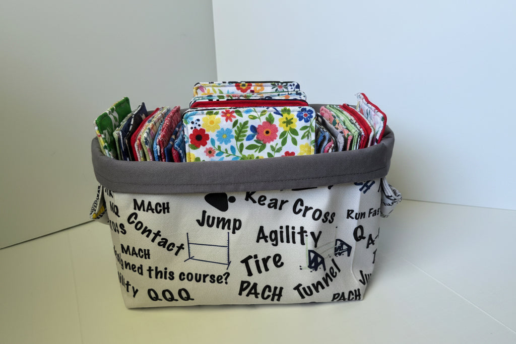 A fabric storage basket with a gray top rim and base, filled with packaged items. The basket body is off-white with black athletic-themed text and graphics, including 'MACH', 'Contact', 'Jump', 'Agility', 'Tire', and 'PACH'.