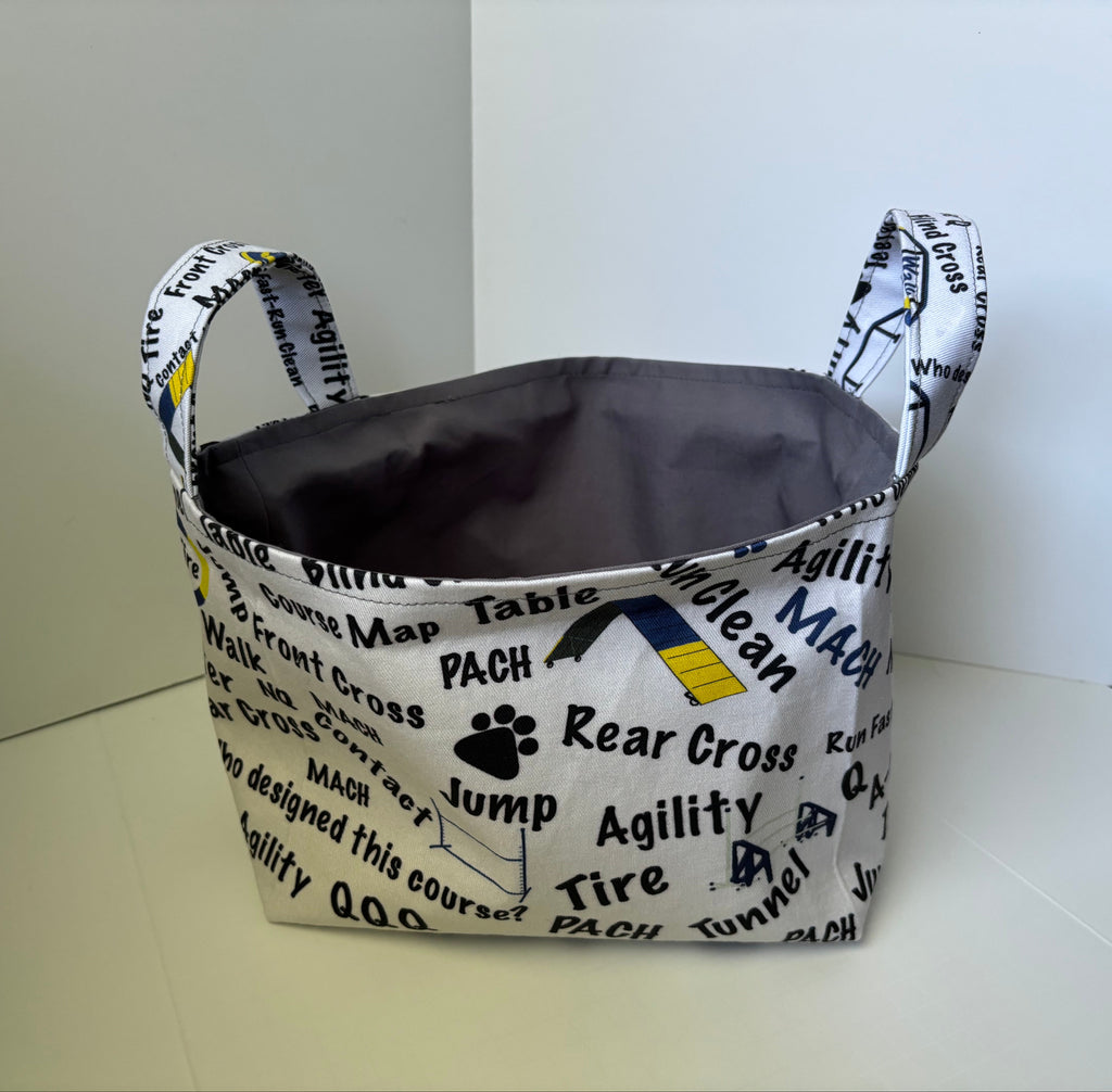 A fabric storage basket with dual handles, featuring a white printed exterior with black text and graphics related to cross country running, and a dark gray interior.