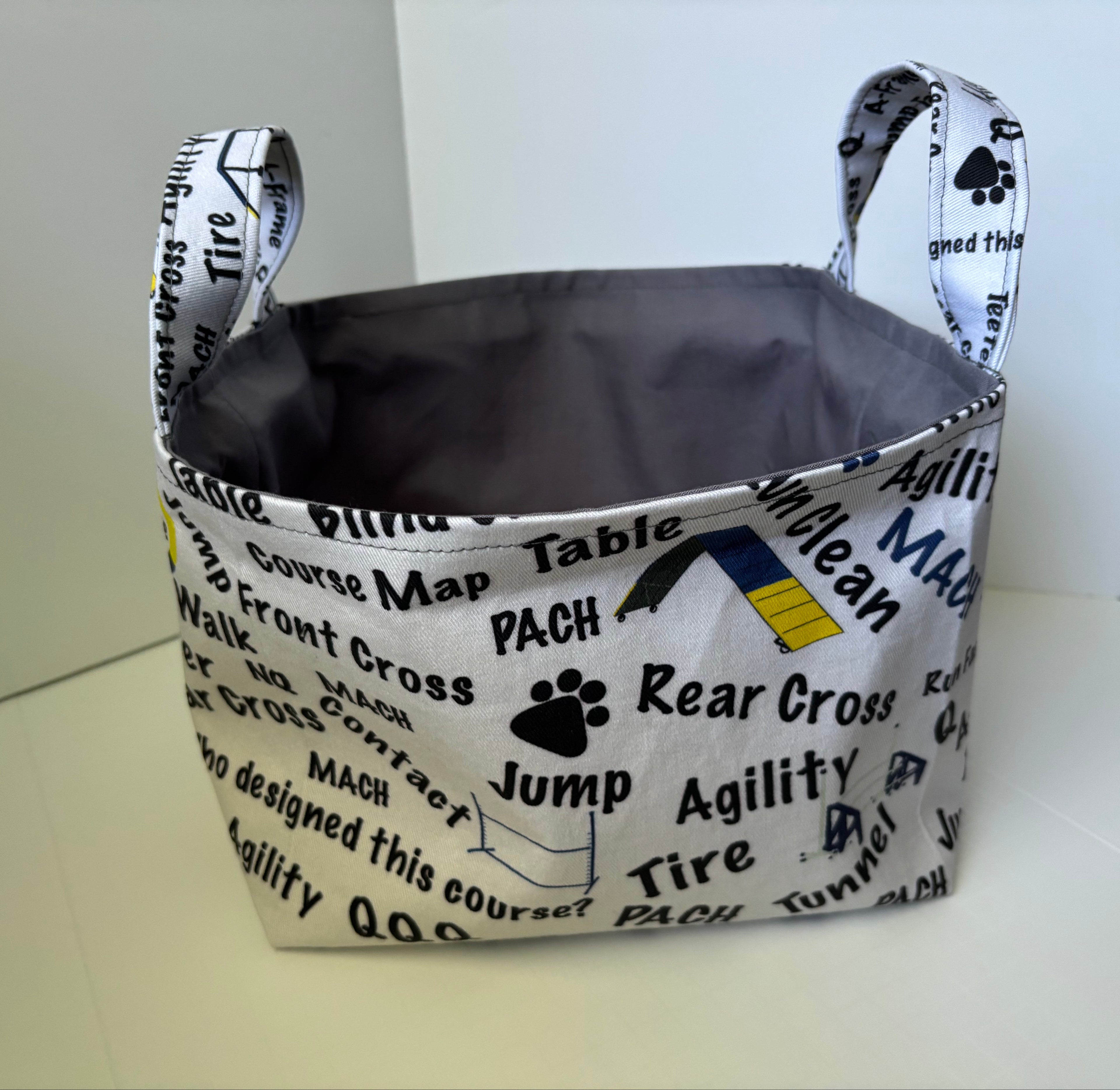 A fabric storage basket with handles, featuring a white printed exterior with black text and graphics related to dog training, and a dark gray interior.