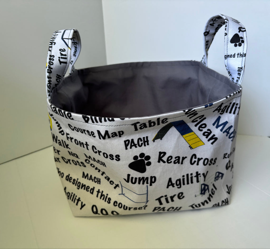 A fabric storage basket with handles, featuring a white printed exterior with black text and graphics related to dog training, and a dark gray interior.