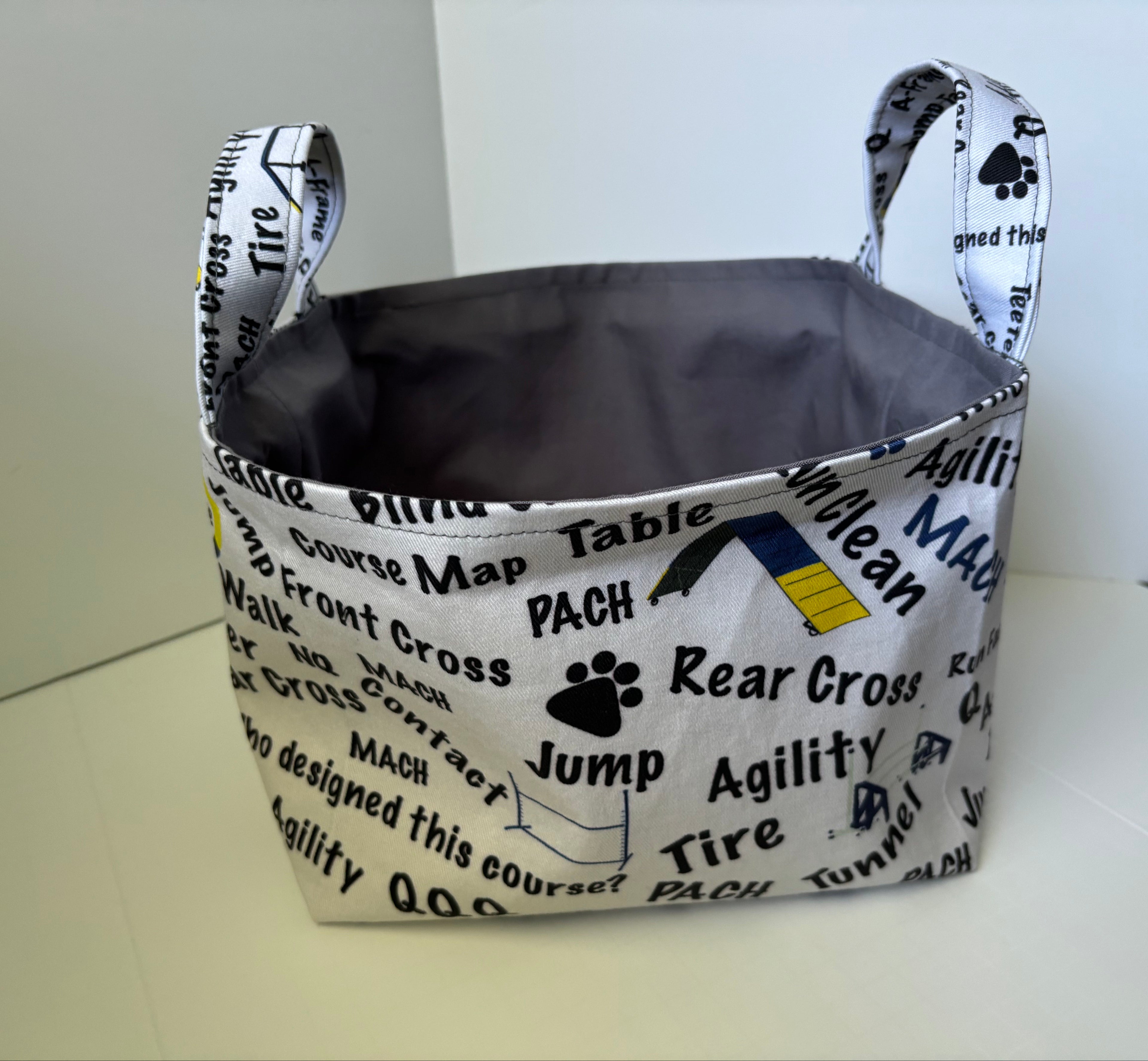 A fabric storage basket with handles, featuring a white printed exterior with black text and graphics related to dog training, and a dark gray interior.