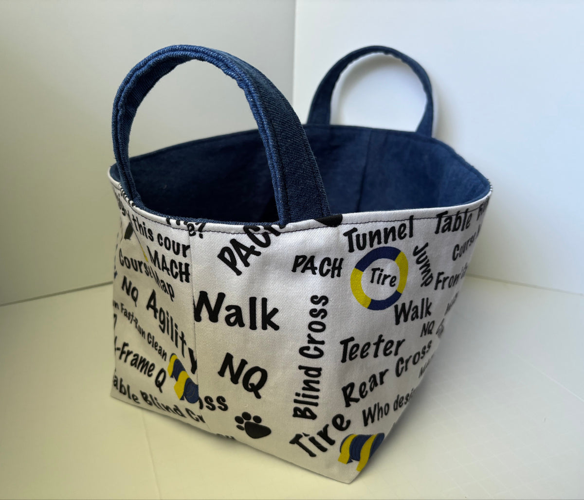 A fabric storage basket with a white exterior printed with black road signs and words like 'PACH', 'Walk', 'Tunnel', and 'Blind Cross', and a blue interior with dark blue handles.