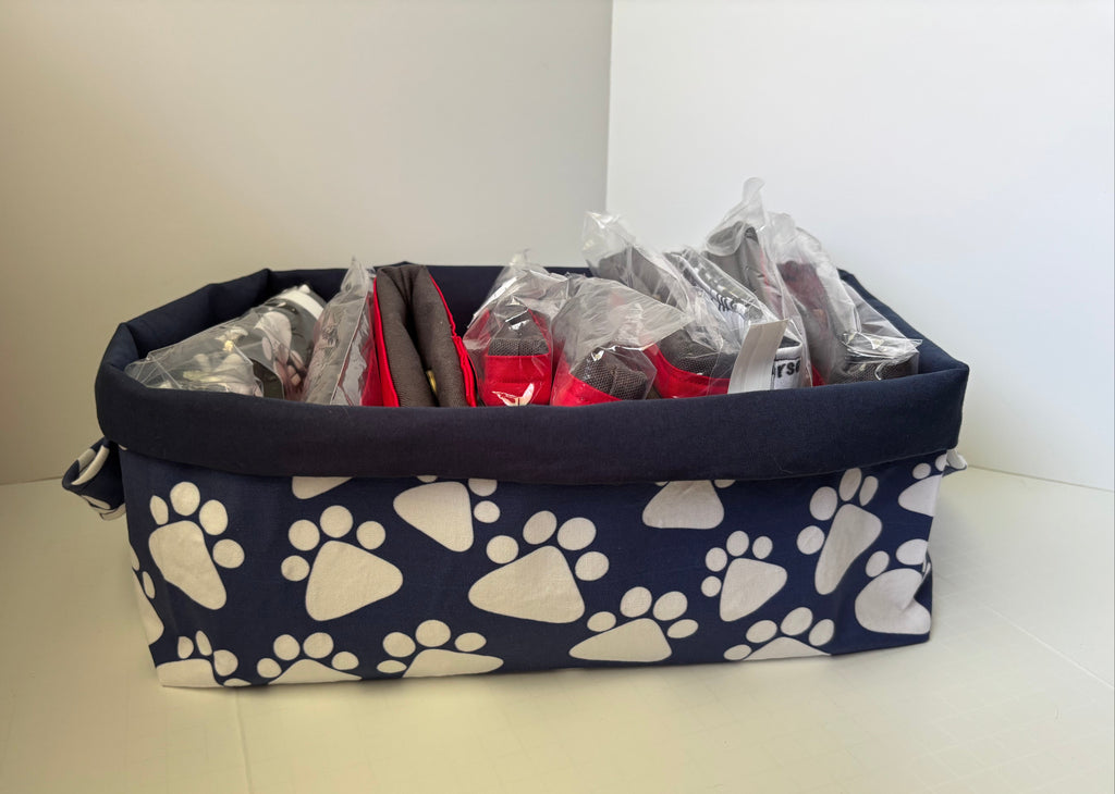 A fabric storage basket with a navy blue base printed with white paw prints, holding various packaged items inside.