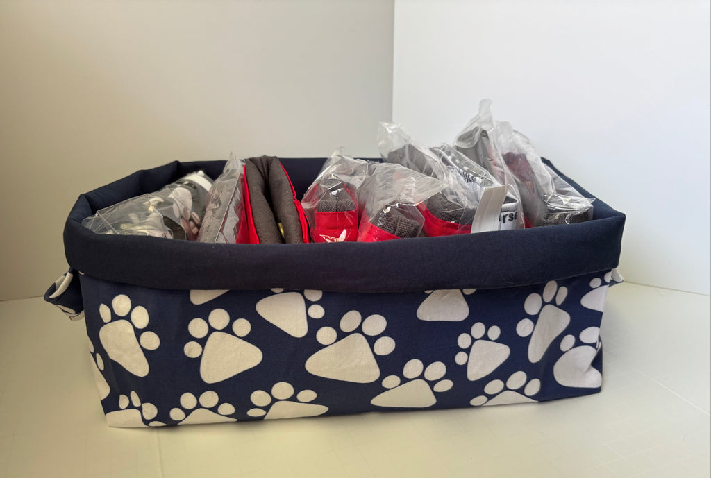 A fabric storage basket with a navy blue base printed with white paw prints, containing several packaged items inside clear plastic bags.