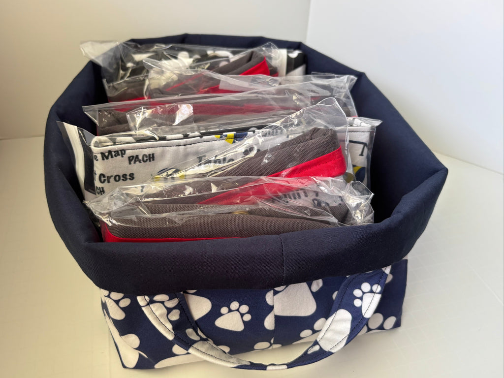 A navy blue fabric storage basket with white paw print patterns on the bottom, filled with several packaged items in clear plastic bags.