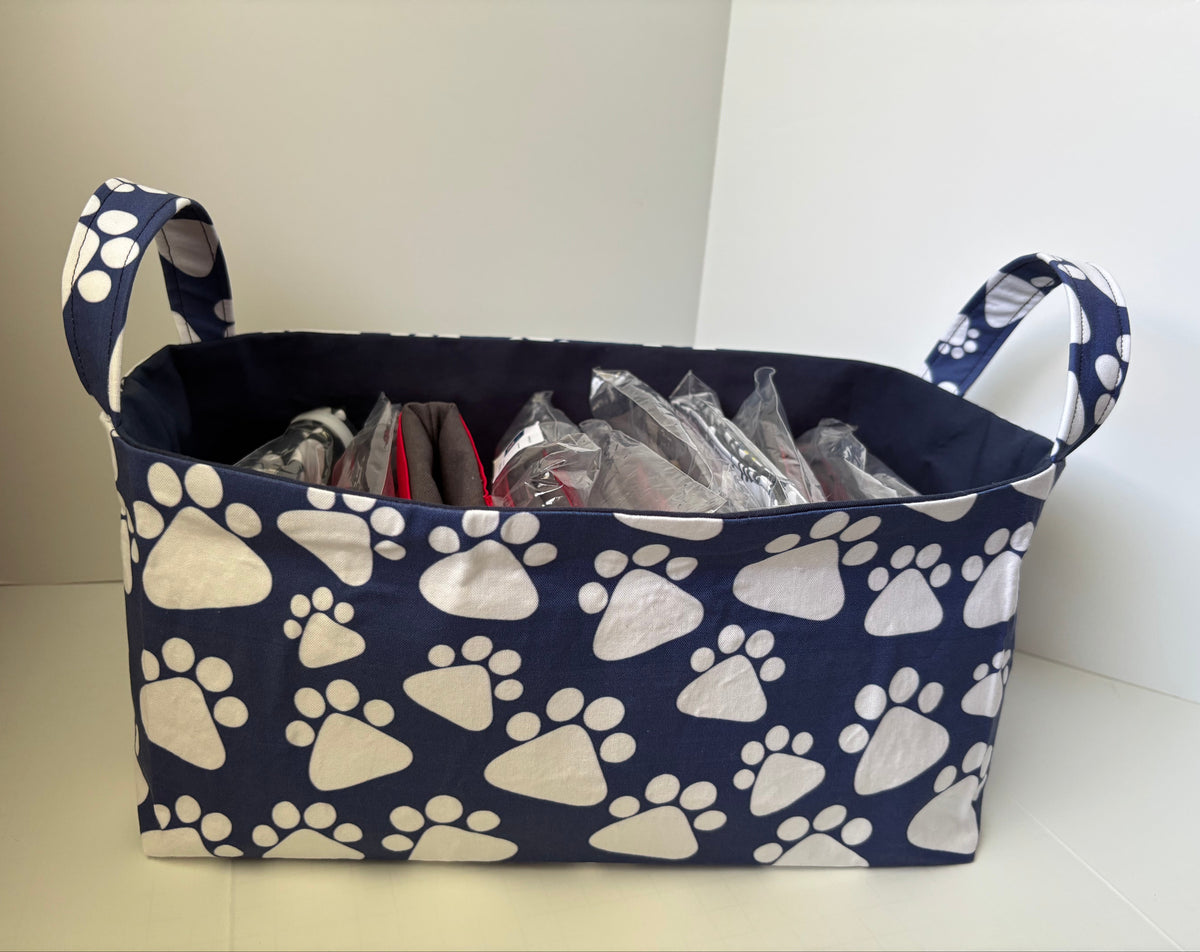 A fabric storage basket with a navy blue and white paw print pattern, shown filled with various items inside clear plastic bags.