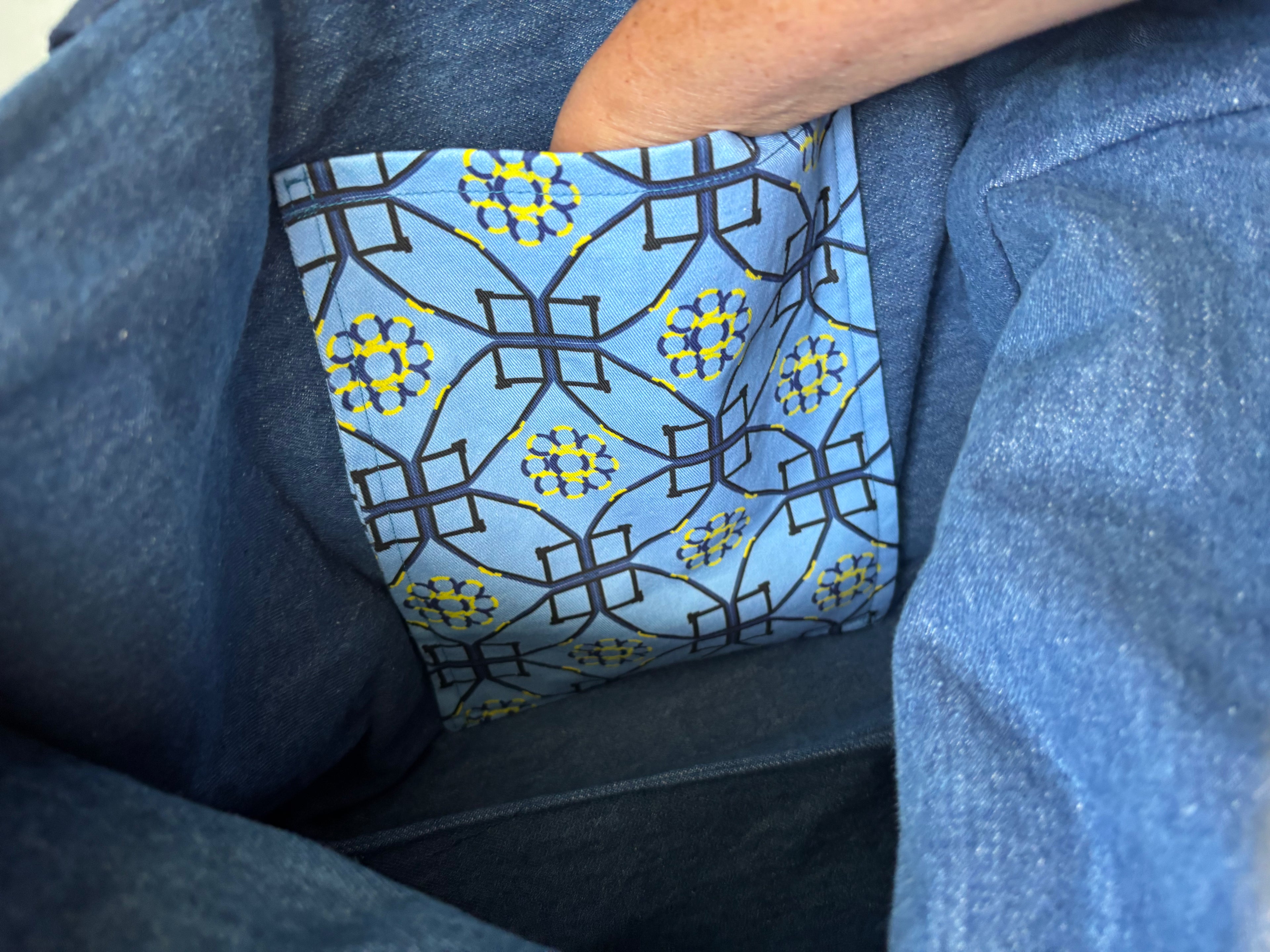 Close-up of a blue patterned fabric lining inside a blue denim or canvas bag, with part of a person's arm visible at the top.