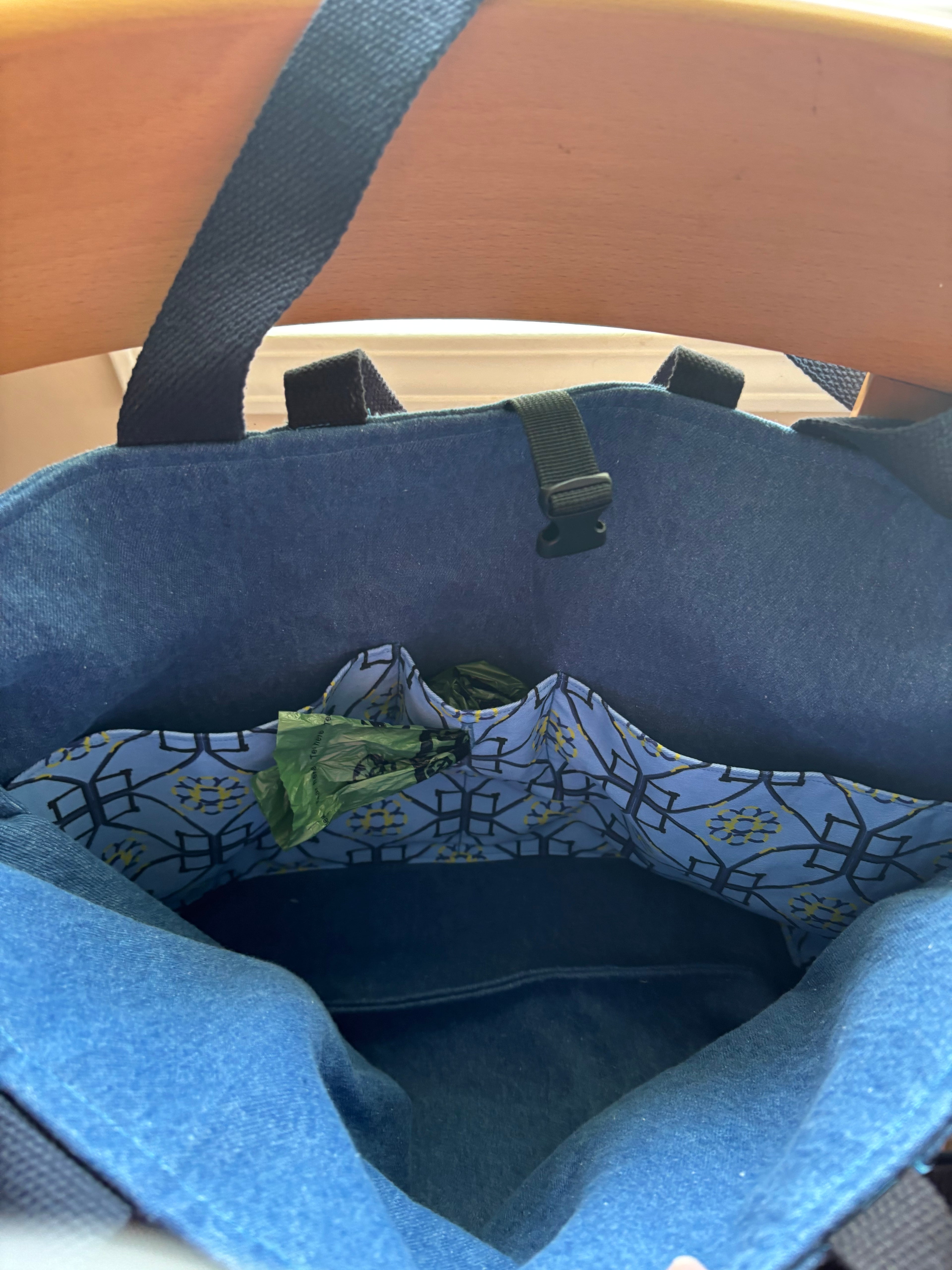 An open blue fabric tote bag with a patterned interior organizer pocket containing a roll of poop bags, photographed from inside looking out.