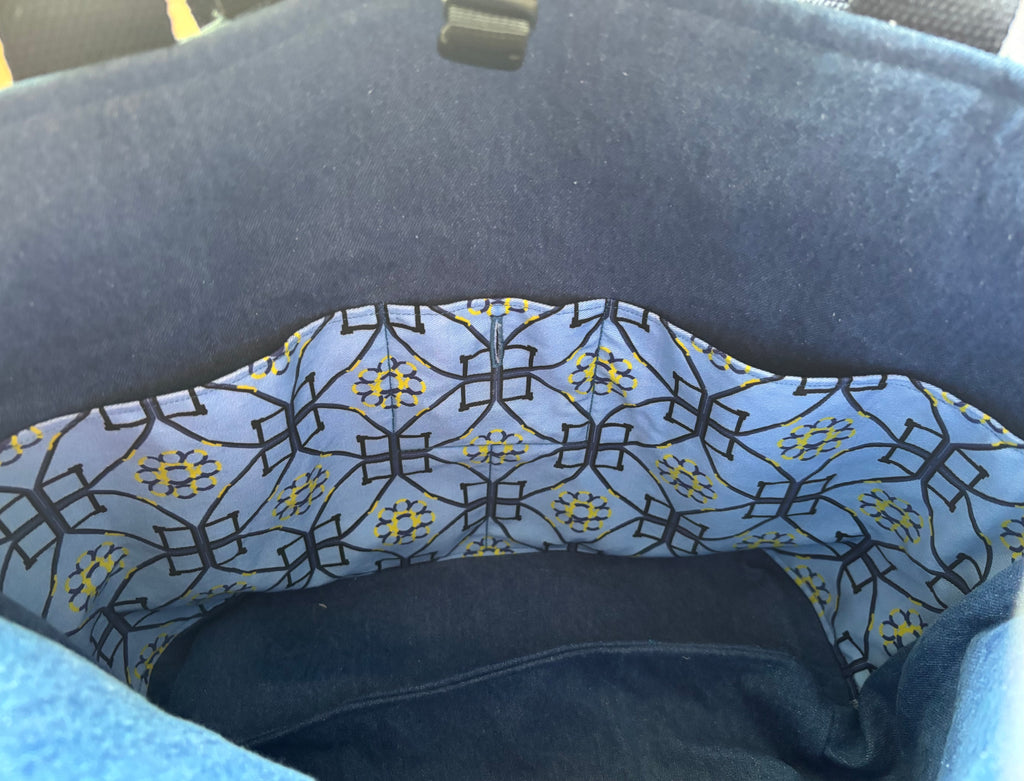 Close-up of the interior lining of a dark blue bag or basket, featuring a light blue dog agility patterned fabric with black geometric lines and small yellow floral accents.