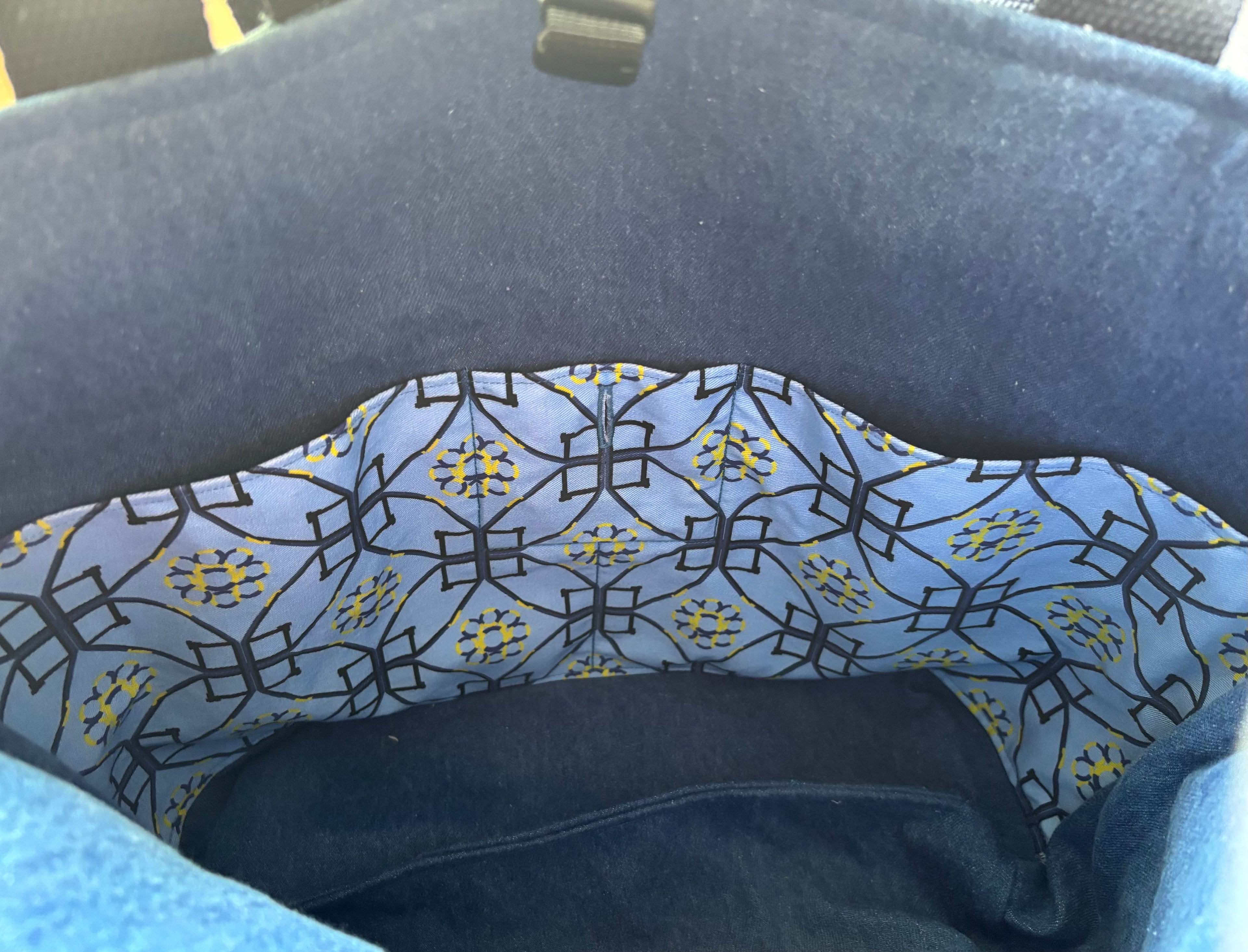 Close-up of the interior lining of a dark blue bag or basket, featuring a light blue dog agility patterned fabric with black geometric lines and small yellow floral accents.