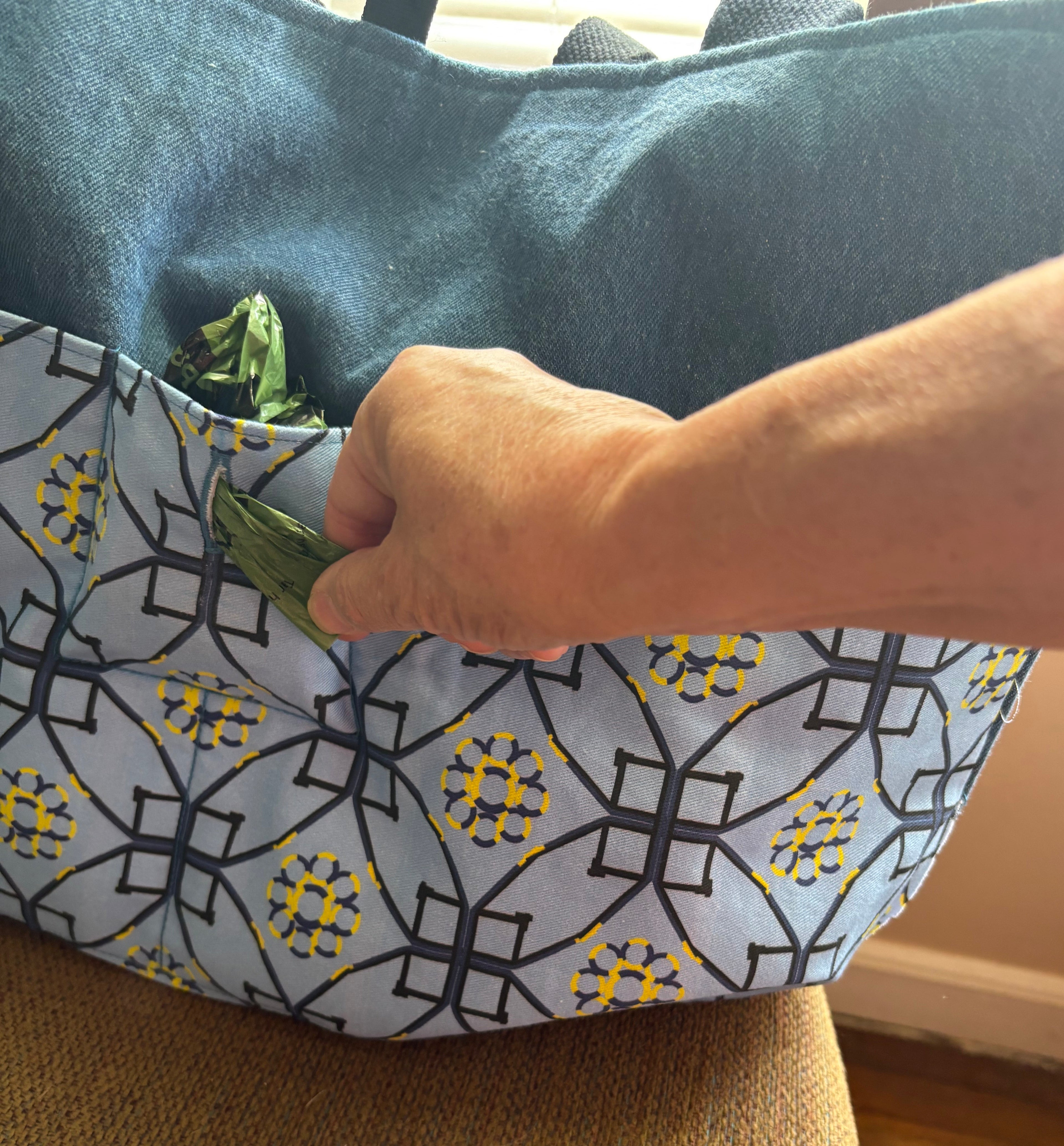 poop bag being pulled off a roll through a button hole in the tote bag pocket. 