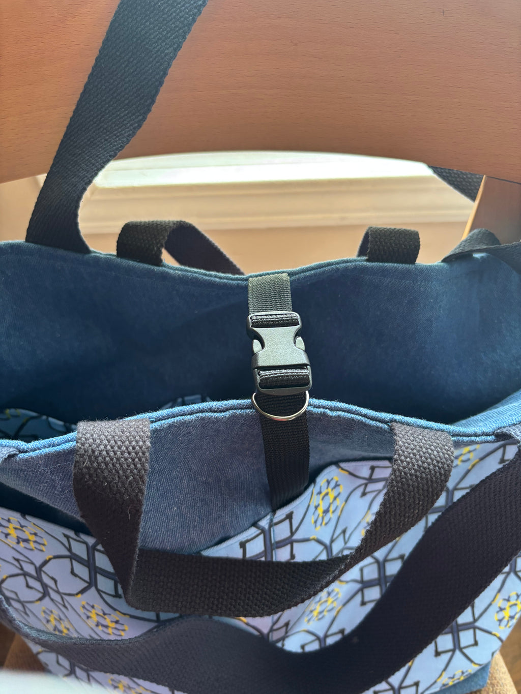Close-up of a tote bag with a blue patterned dog agilityexterior, dark blue fabric lining, and black webbing straps with a plastic buckle closure.